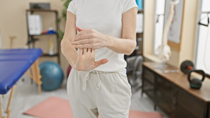Fototapeta premium Mature woman exercises wrist in physiotherapy clinic with equipment background, portraying healthcare and rehabilitation.