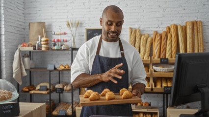 Handsome young african american man holding tray of croissants in indoor bakery shop