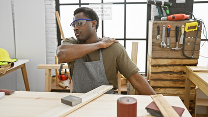 African american man experiences shoulder pain while working in a carpentry workshop