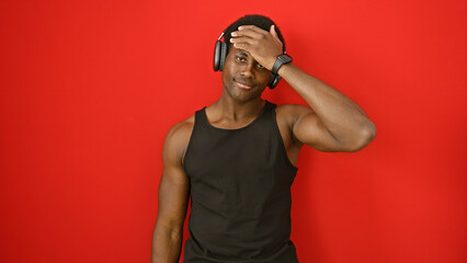 Young african american man with headphones stands against a vibrant red background, exuding coolness and confidence.