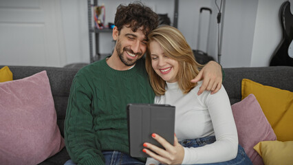 Smiling couple cuddled on a sofa using a tablet in a cozy living room.