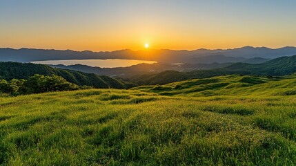 Fototapeta premium Rolling green hills of Kurumayama Plateau with a distant view of Lake Shirakaba reflecting the golden hues of the setting sun.