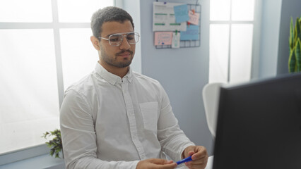 Fototapeta premium Young man working in an office setting, focusing intently on his task while seated at his desk in a bright, modern workplace environment.