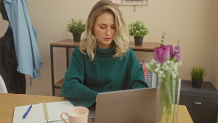 Caucasian blonde woman working on laptop in home office with plants and coffee mug