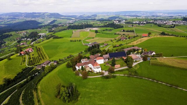 A cinematic aerial view of the Capuchin convent Maria Hilf in Zug in Switzerland surrounded by vast lush green farmland and the picturesque Alpine countryside