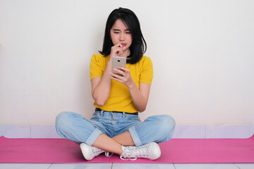 A woman sitting cross legged looking at her phone with worried expression