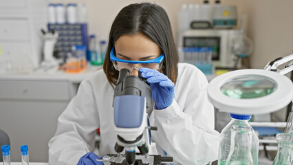 Focused hispanic woman scientist using microscope in a modern laboratory setting.