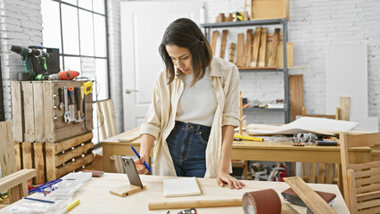 A focused young woman sketching a design in a bright and organized carpentry workshop.