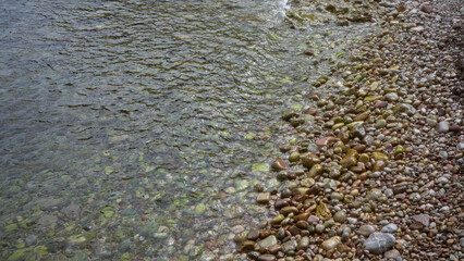 Clear water gently laps over colorful pebbles on a serene beach, creating a tranquil natural scene...