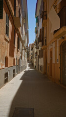 Narrow street in palma mallorca with historic buildings and balconies, shaded passageway providing a tranquil ambiance in the mediterranean city under a clear blue sky