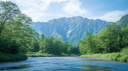 Fototapeta premium The peaceful Azusa River flowing through Kamikachi, framed by fresh green trees and the towering peaks of the Hotaka Mountains in the distance.