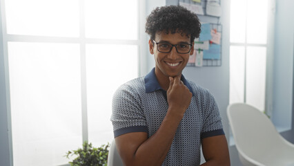 Fototapeta premium Young man smiling in a bright office, creating a positive and welcoming environment in a professional workspace with modern decor and natural light.