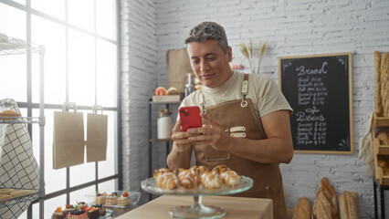 Young man taking photo of pastries with smartphone in bakery shop interior with displayed breads and sweets on background