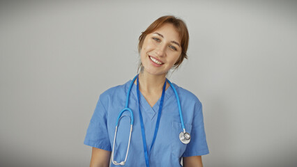 Portrait of a smiling young caucasian woman in blue scrubs with a stethoscope against a white...