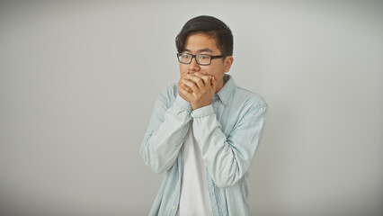 Obraz premium A young asian man with glasses covers his mouth against a white background, conveying surprise or secrecy.