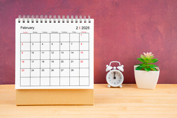 February Monthly desk calendar for 2025 year and alarm clock on wooden table.