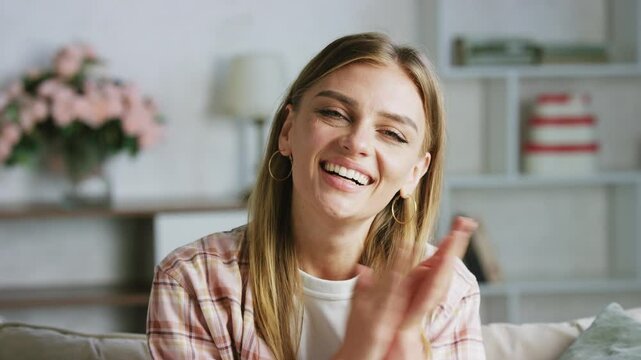 Happy woman claps her hands and smiles while sitting on a cozy sofa in a bright living room. Joy radiates as she expresses excitement and appreciation in a relaxed atmosphere
