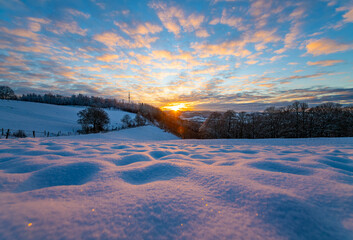 Winter sunset panorama in Iserlohn Germany with snow covered meadow and colorful blue sky creating...