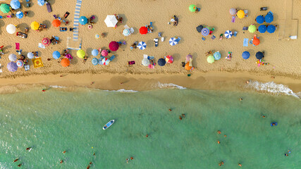 Aerial perpendicular view of people vacationing on the beach of San Pietro in Bevagna, in Salento, Puglia, Italy. There are many beach umbrellas on the shore of that public beach. Holidays concept.