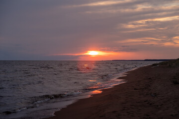 The sun sets on the horizon, casting warm colors across the water as gentle waves wash onto the sandy beach