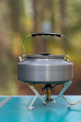 A gleaming kettle sits atop a portable stove, surrounded by a tranquil forest, inviting moments of outdoor brewing