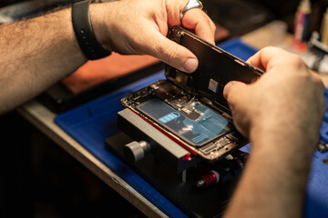 Technician repairing smartphone battery in workshop with tools and equipment during daytime