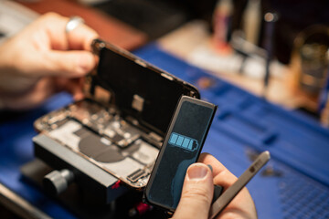 Expert technician repairing a smartphone battery in a well-equipped workshop with precision tools during daytime