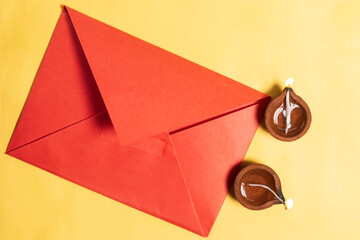 Happy Diwali celebration with red cover and two burning diyas filled with oil on yellow background.