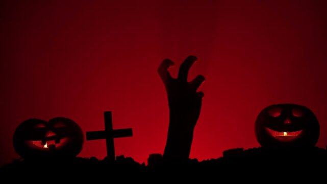 Scary dirty halloween zombie hand silhouette raising from grave points finger up shows thumb up, isolated on red background. Mystery halloween concept.