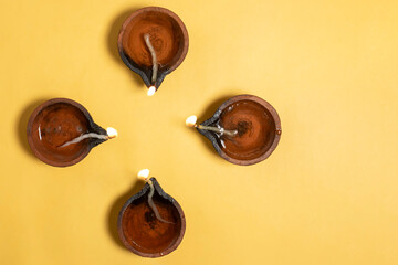 Happy Diwali - Overhead view of glowing clay diyas on vibrant yellow background with space for text