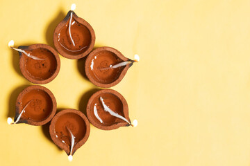 Traditional clay diya lamps are lit in a floral pattern on a yellow background during Diwali festival celebrations.