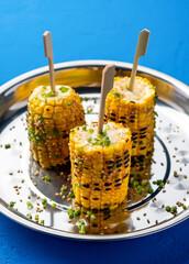 Grilled Butter Corn on the Cob with Sesame Seeds Herbs, and Green Onion served in plate isolated on blue background closeup side view food
