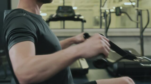 Midsection shot of male athlete pulling cables on seated row machine while exercising in gym