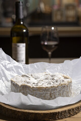 Camembert cheese on a wooden cheese board with wine in the  .background.