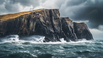 Fototapeta premium A rocky island with steep cliffs rising from the ocean, surrounded by rough waves and stormy skies.