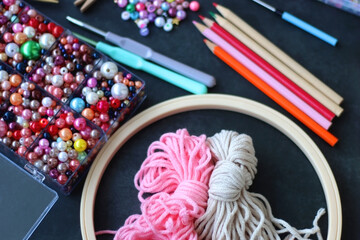 Colorful beads, coloring pencils, glitter, needles, string, hoop, tape and scissors on dark...