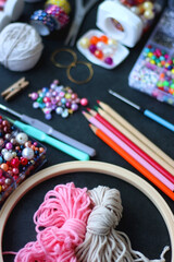 Colorful beads, coloring pencils, glitter, needles, string, hoop, tape and scissors on dark...