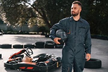 Standing and holding safety helmet. Man is outdoors, kart racing conception