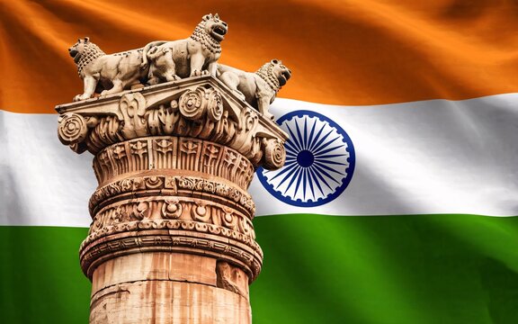 A pillar of the Ashoka Stambh with a waving Indian flag behind it.