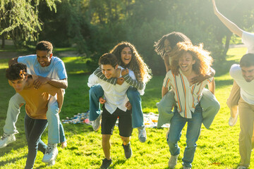Group of friends running through park giving piggyback rides