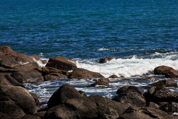 Fototapeta premium Large waves crash into coastal rocks. Dramatic sea shore background. Raglan, New Zealand
