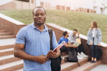 Fototapeta premium African American Confident Student Holding Books Outdoors with Friends on Campus Steps