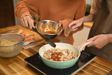 Close up shot of young couple cooking, stirring ingredients in frying pan with wooden spatula
