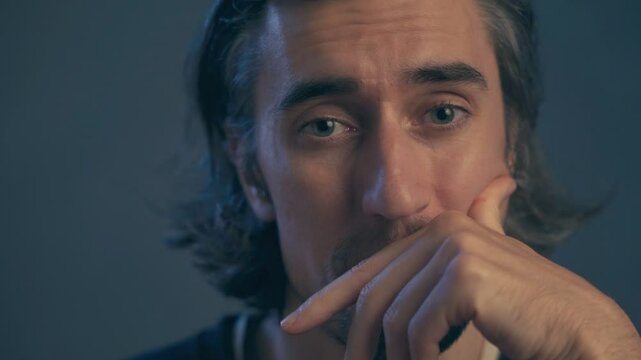 a young man with long hair, large expressive eyes, European appearance, thick black eyebrows, dark-skinned, puts his head on his palm, sighs negatively, shakes his head, doesn&rsquo;t believe what he&rsquo;s bein
