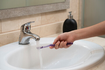 toothbrush in the sink held by an unrecognizable hand