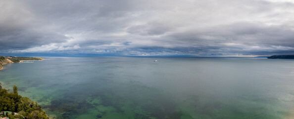 A panoramic view of a vast ocean under a dramatic, overcast sky. A distant ship on the horizon enhances the feeling of isolation and vastness. Ideal for seascape and maritime themes
