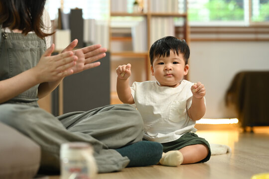 Happy mother playing with cute little baby boy on a wooden floor at home. Child care concept