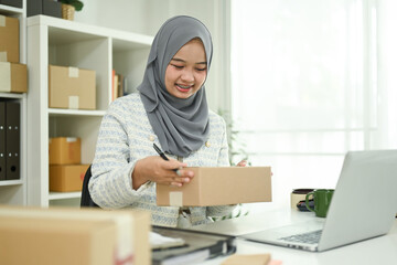 Young Muslim female entrepreneur packing parcels for delivery. E-commerce concept