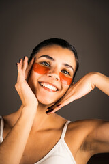 Fototapeta premium Young woman with perfect glowing skin and natural makeup posing for the camera with medical collagen patches under her eyes to reduce fatigue and puffiness. Skin care.Modern beauty tools concept