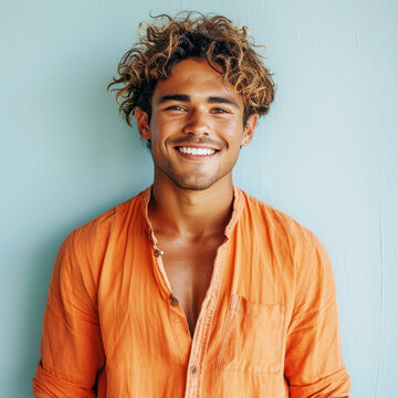 Portrait of a smiling sandy-haired young male wearing an orange shirt, standing against a light blue background